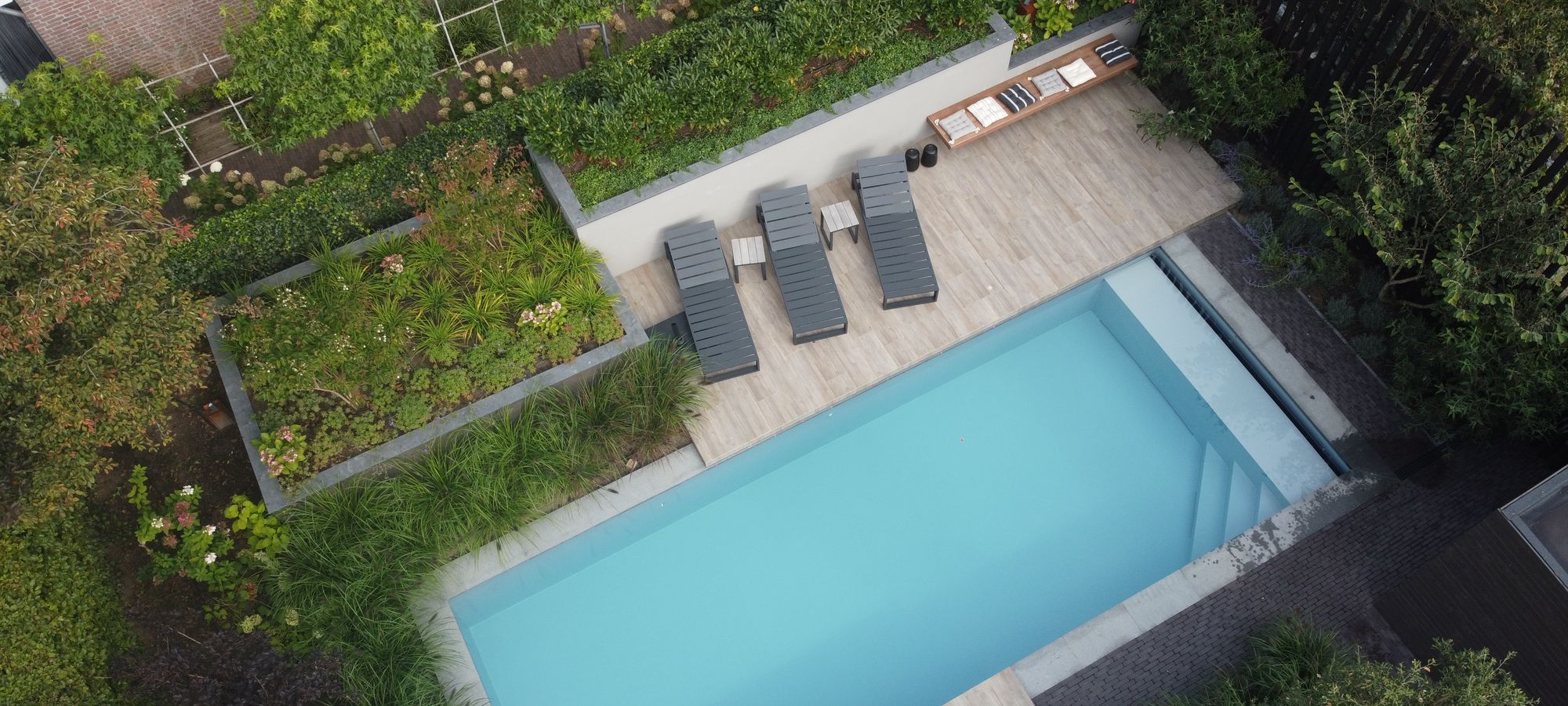 Zwembad met terras en ligbedden in een tuin met beplanting, van boven gefotografeerd