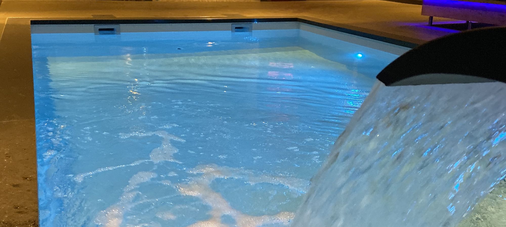 Binnenzwembad met verlichte waterval in een wellnessruimte