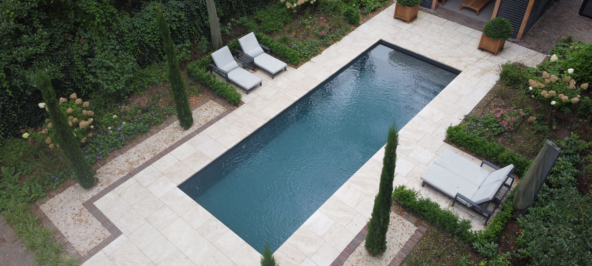 Donker afgewerkt bouwkundig zwembad in een strak aangelegde tuin, van boven gefotografeerd